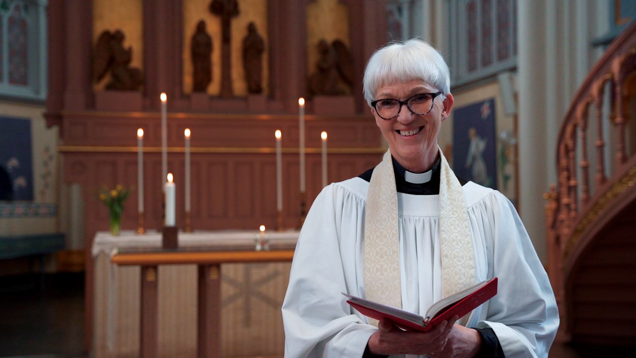 Kvinna i prästkläder framför altare. 