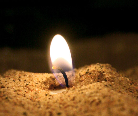 Ljuslåga i sanden, mörk bakgrund