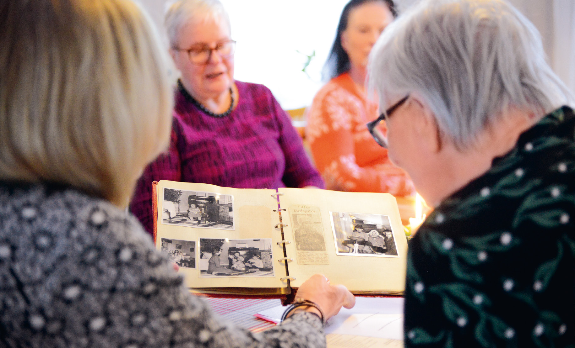 Fyra damer bläddrar i ett gammalt fotoalbum. 