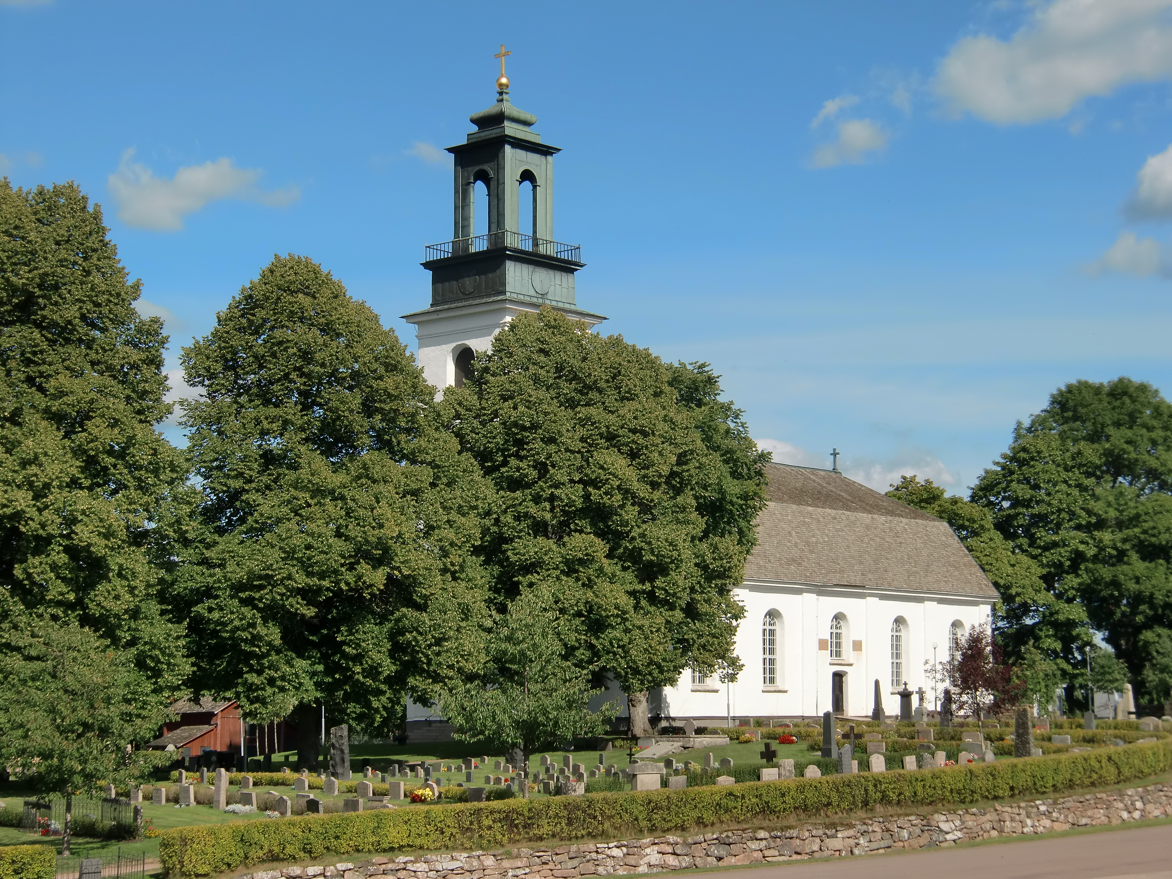 Vitputsad kyrka omgiven av träd och kyrkogård.