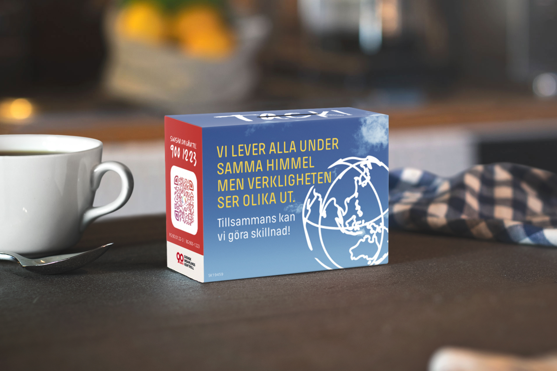 Fastebössa som uppmanar till gåva står på ett bord bredvid en kaffekopp. 