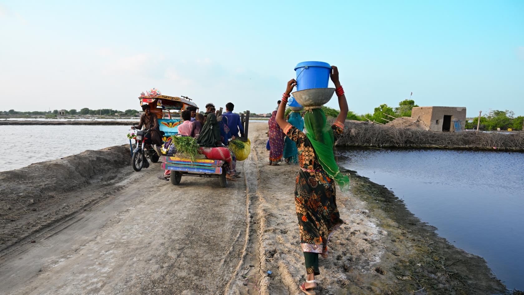 1.	A man riding a motorbike, a bunch of people riding a cart and three women walking on a road. 