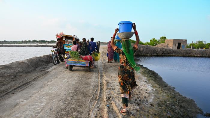 1.	A man riding a motorbike, a bunch of people riding a cart and three women walking on a road. 