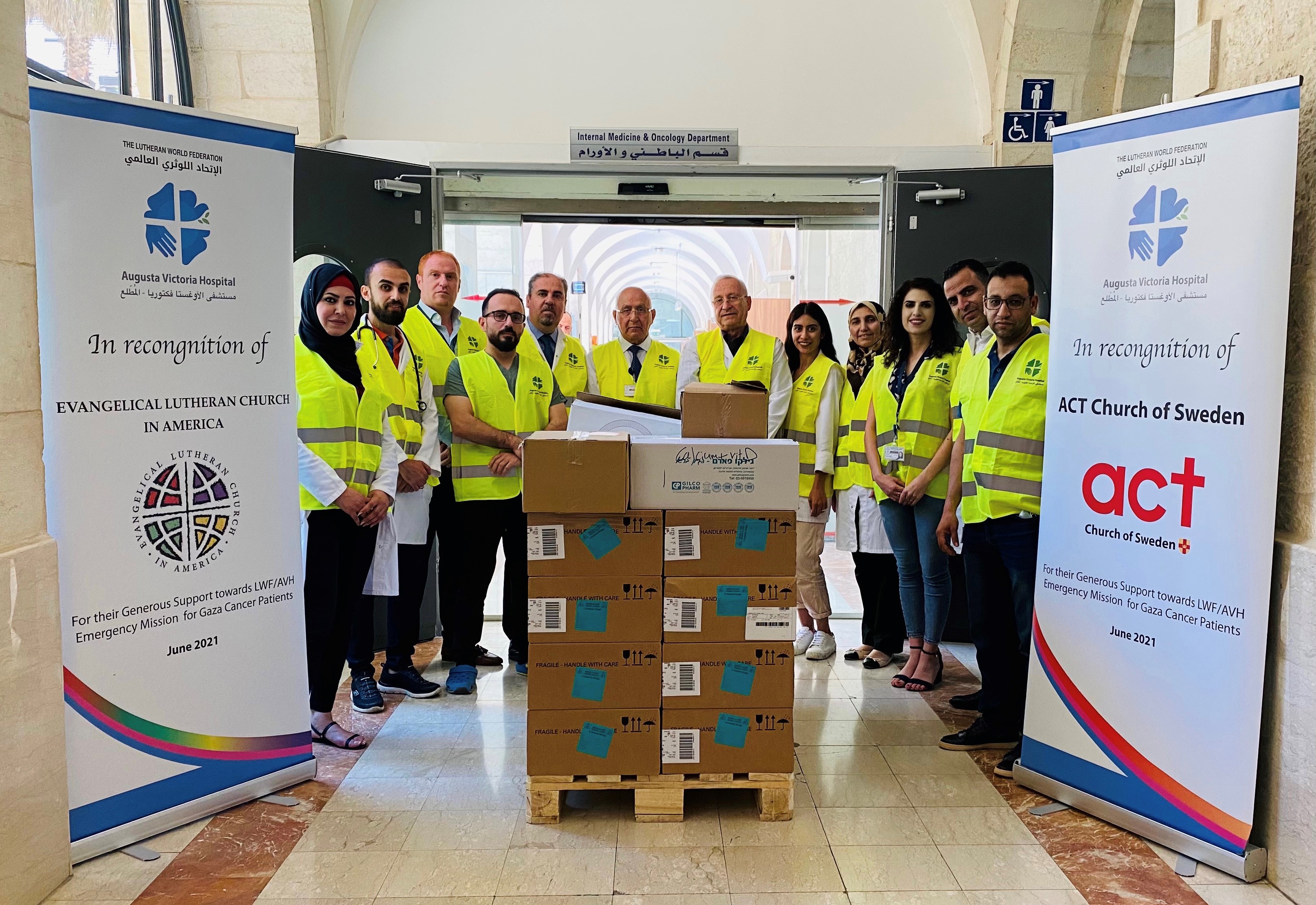 Medicins personal uppradade för gruppbild. 12 personer i gula västar vid en lastpall med medicin. 