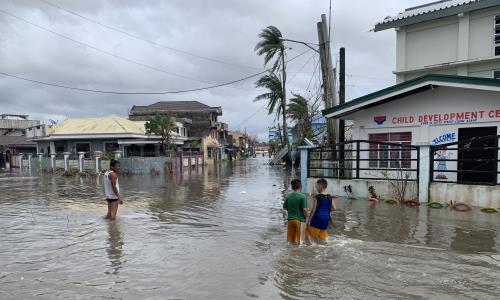 Tre personer står med vatten till knäna på en översvämmad gata.