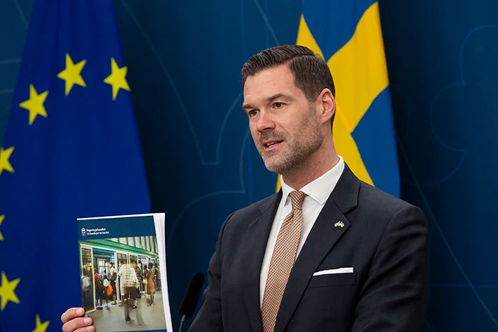 En person står framför Sveriges flagga och EU-flaggan hållandes en text