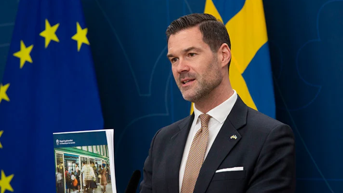En person står framför Sveriges flagga och EU-flaggan hållandes en text