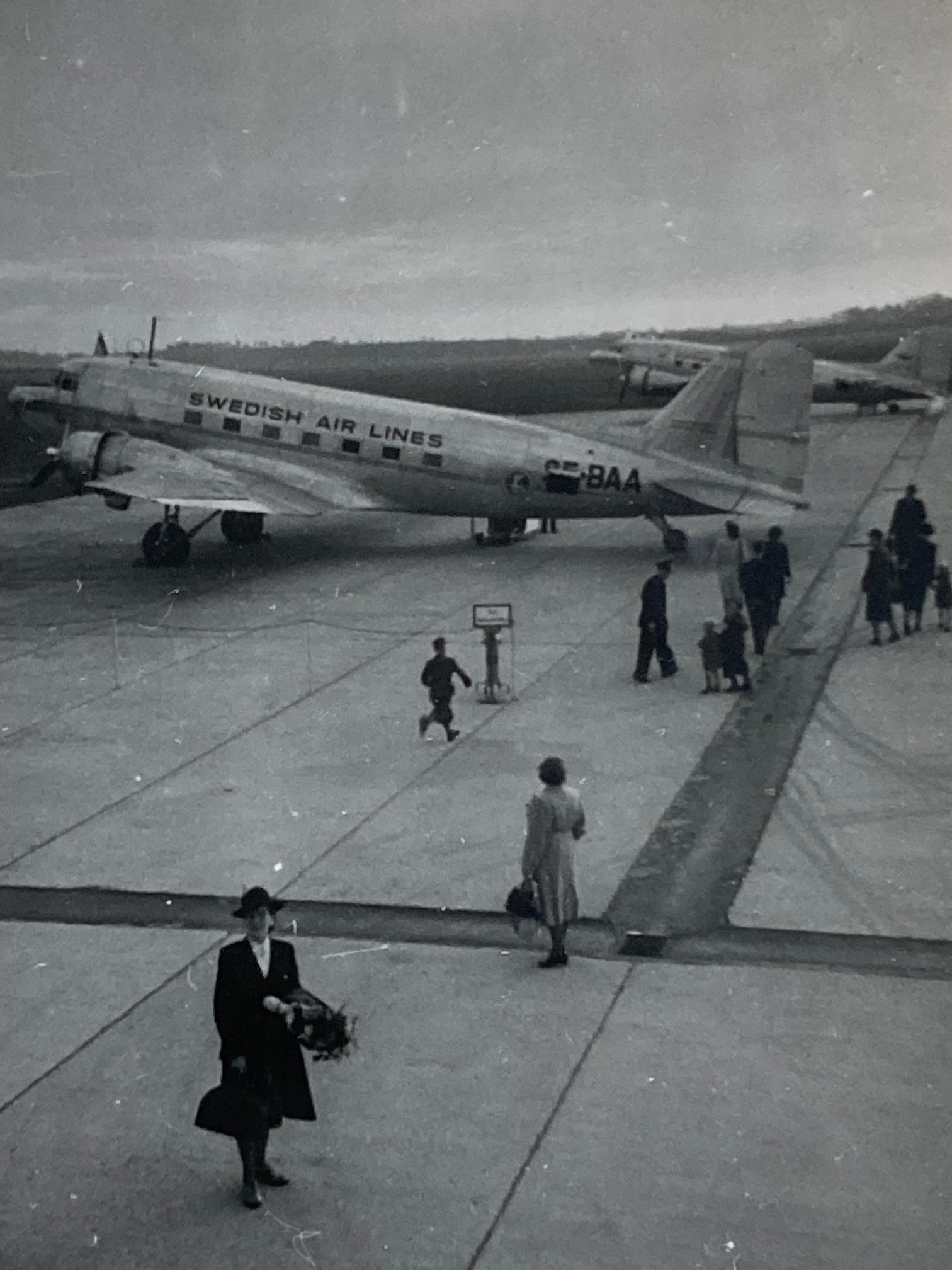En historisk bild från 1946. På bilden syns några personer med resväskor framför ett flygplan. 