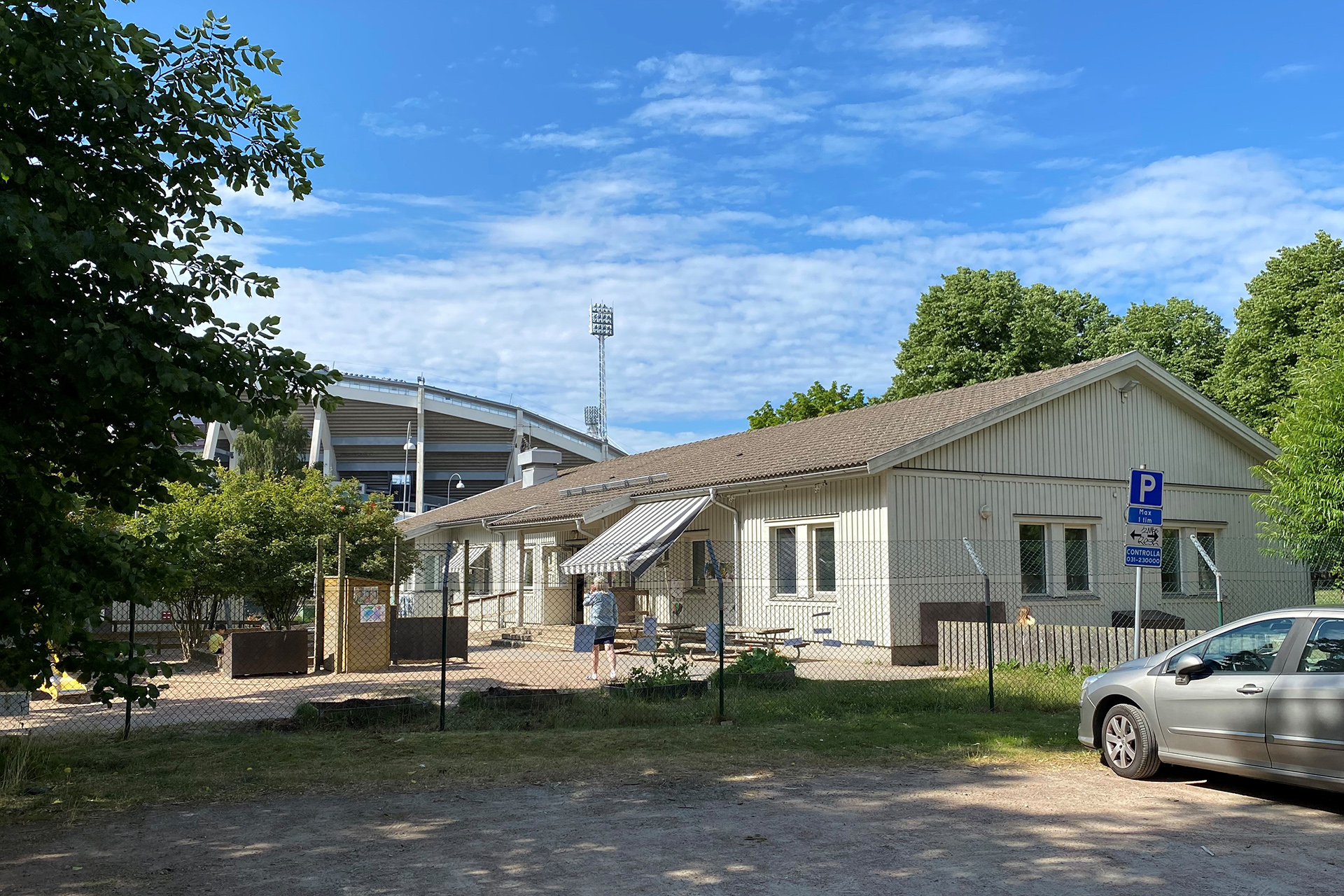 Bild på byggnad med träd runt, blå himmel och en bit av Ulllevi arena i bakgrunden.