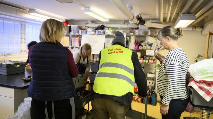 tre personer står med ryggen til mot kameran. de sorterar mat. personen i mitten har en varselväst på sig. 