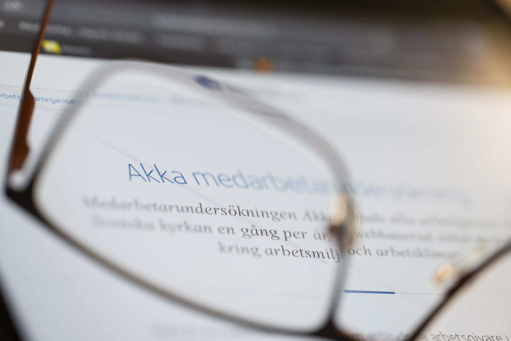 ett par glasögon ligger framför en datorskärm. Genom ena glaset kan man läsa ordet Akka. 