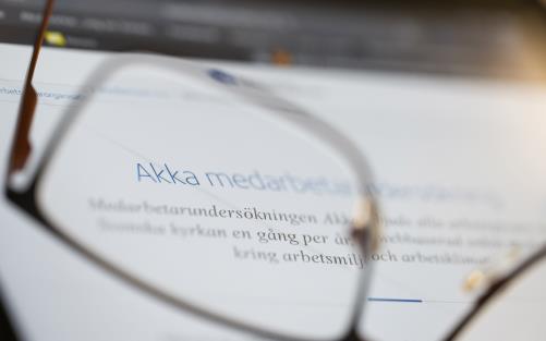 ett par glasögon ligger framför en datorskärm. Genom ena glaset kan man läsa ordet Akka. 