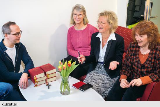Kvinnor sitter och skrattar runt ett bord. På bordet står en vas med tulpaner. 