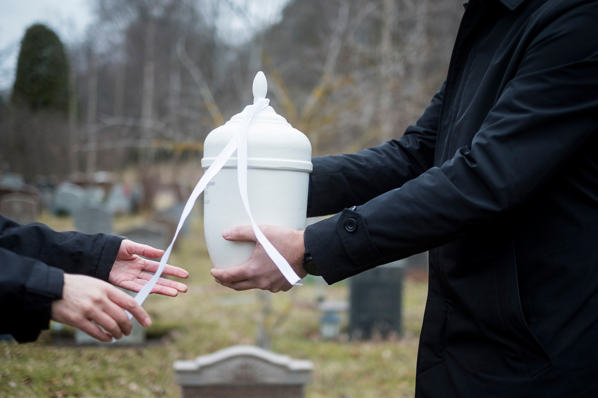 En vit urna som varsamt överräcks mellan två personer.