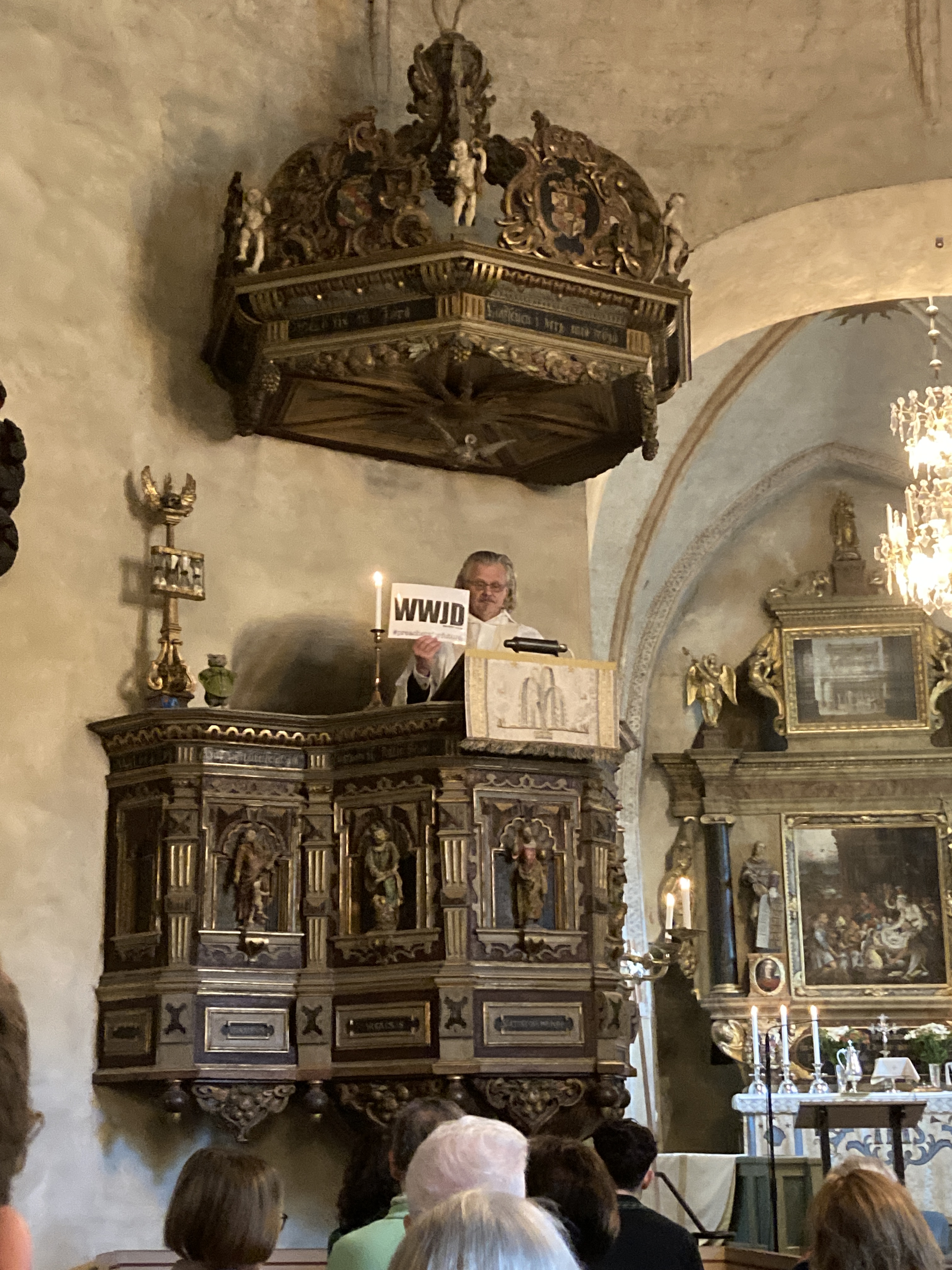 Niklas Lång står i predikstolen i Solna kyrka och håller upp en skylt med texten "WWJD – What Would Jesus Do?".