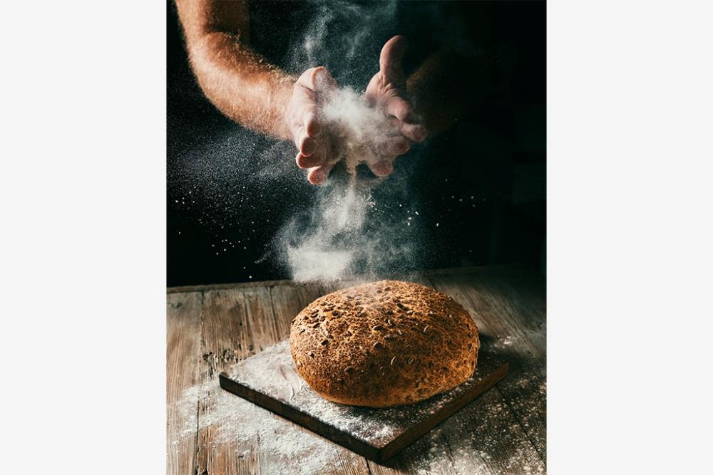 En person häller mjöl på ett bröd. 