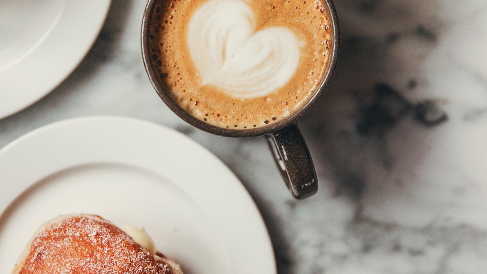 Kaffe med ett hjärta i mitten och en bulle.