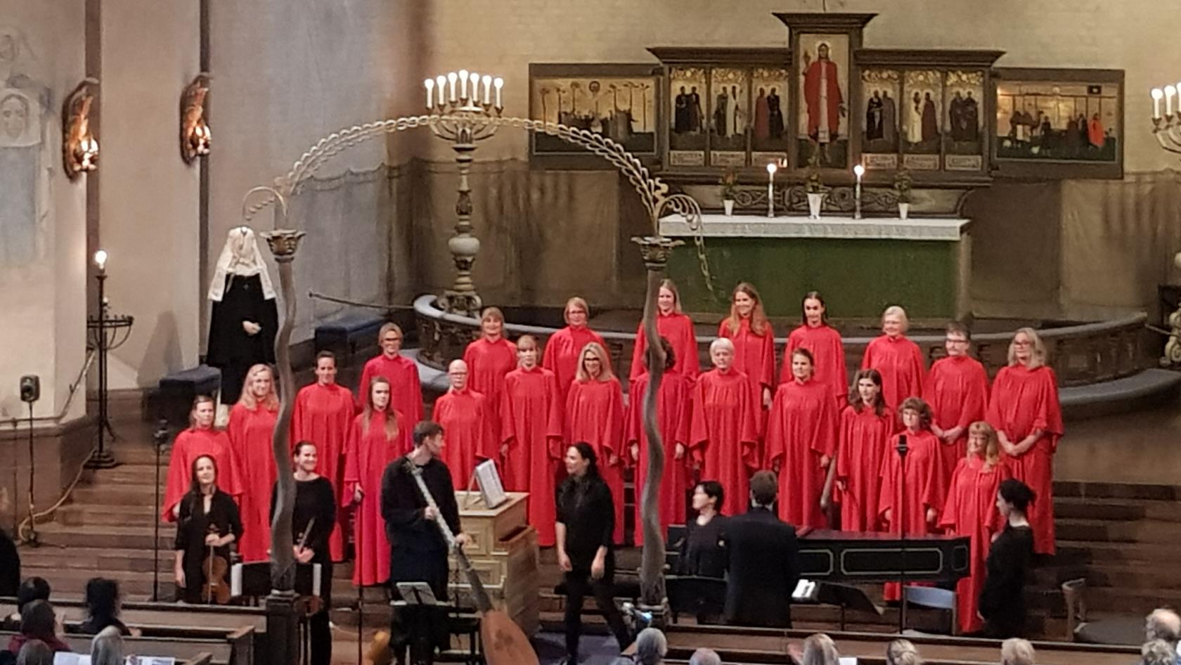 Ett antal personer i röda dräkter, samt några personer utan röda dräkter,  står framför altaret i Högalidskyrkan. 