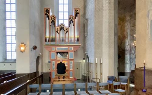 En orgel och en person som sitter vid den. kyrkbänkar, ljus, höga fönster. 