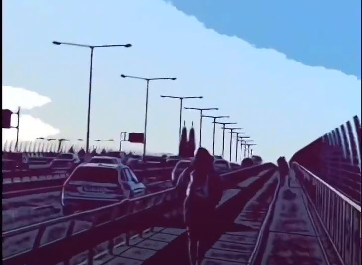 En person går över en bro och flera bilar kör bredvid åt olika håll. 