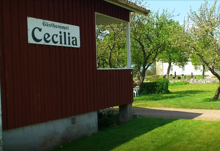 Ett rött hus med veranda sett från sidan och en kyrkogård i bakgrunden