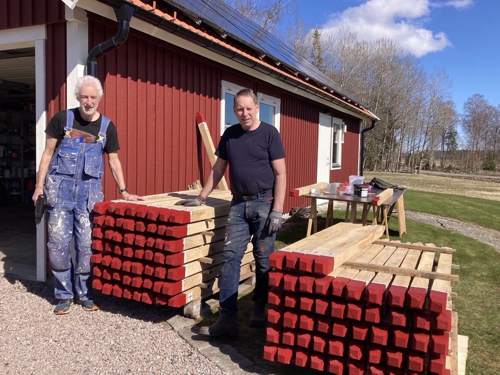 Två män står framför två högar av stolpar med rödmålade toppar.