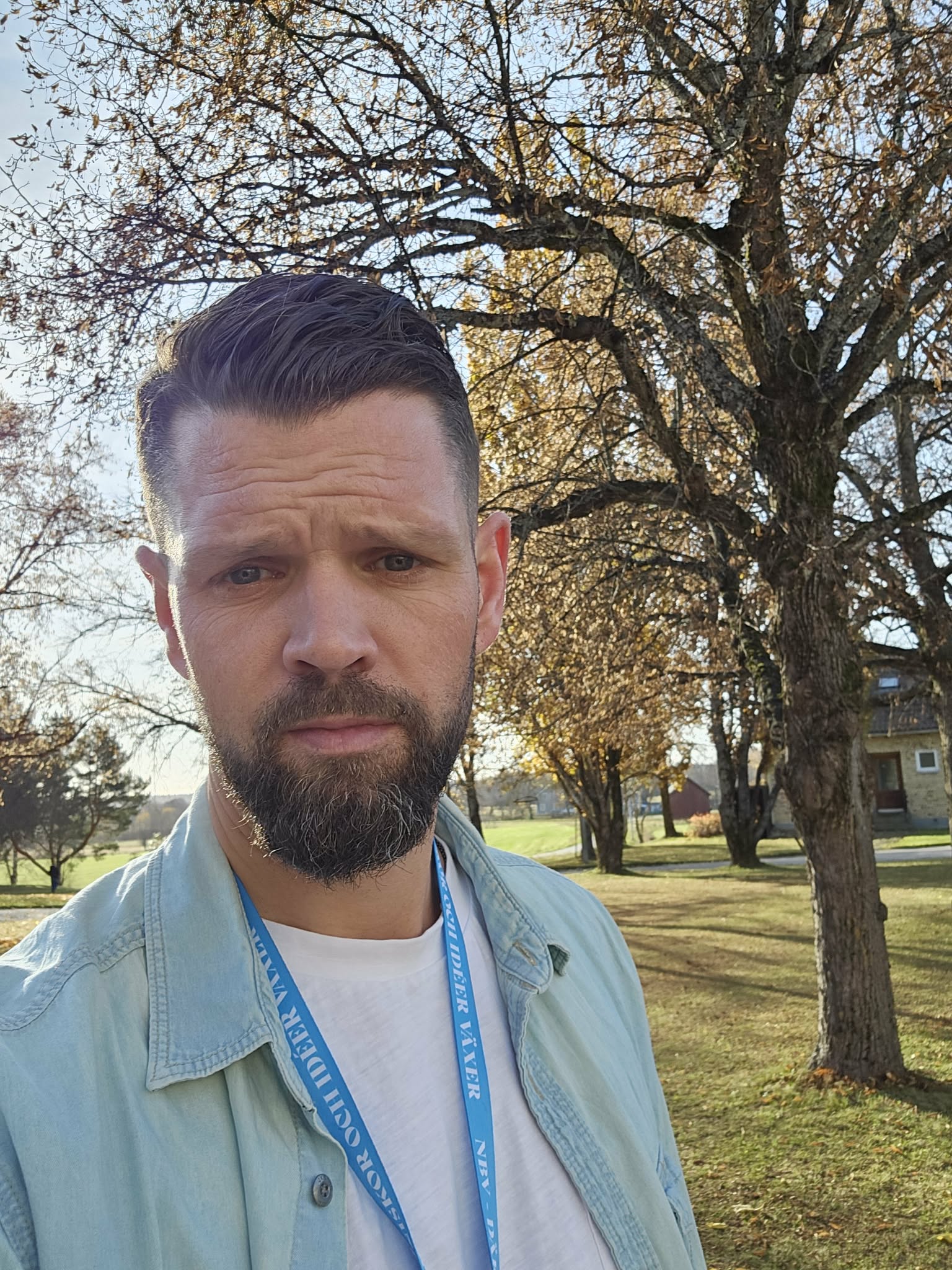 Bilden visar en man som heter Johan Jakobsson. Han har mörkt hår, skägg och mustasch. Han har en vit t-shirt med en uppknäppt jeansskjorta eller jacka över.