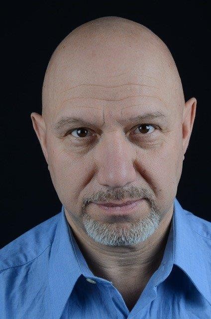 En medelålders man med kort skägg och mustasch, kalt huvud och blå skjorta