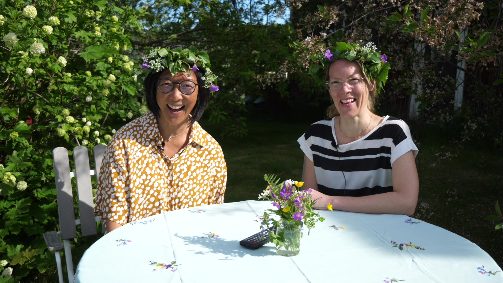 Åsa och Anna på söndagsskolan Barnens stund sitter i en trädgård med midsommarkransar på huvudet.