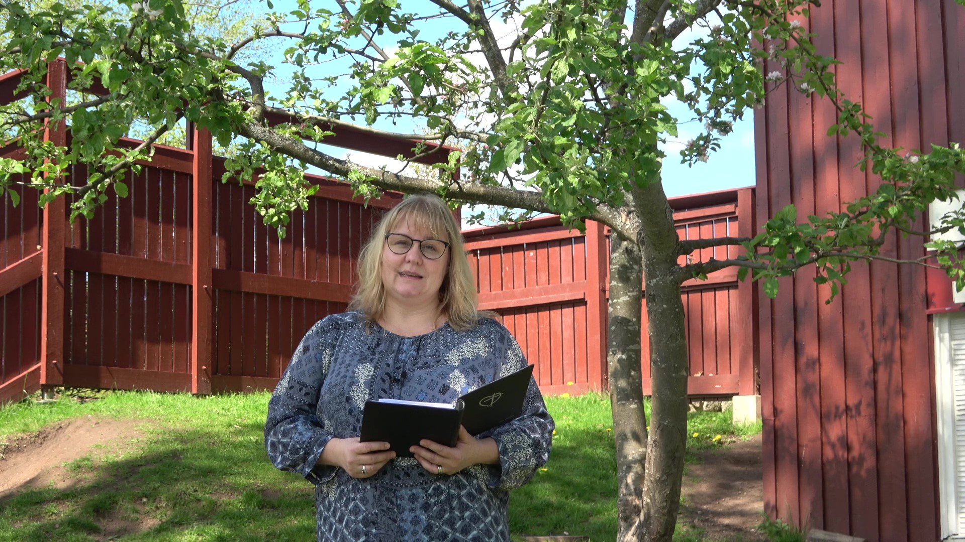 Prästen Maria Liljenberg står under ett grönskade öppelträd