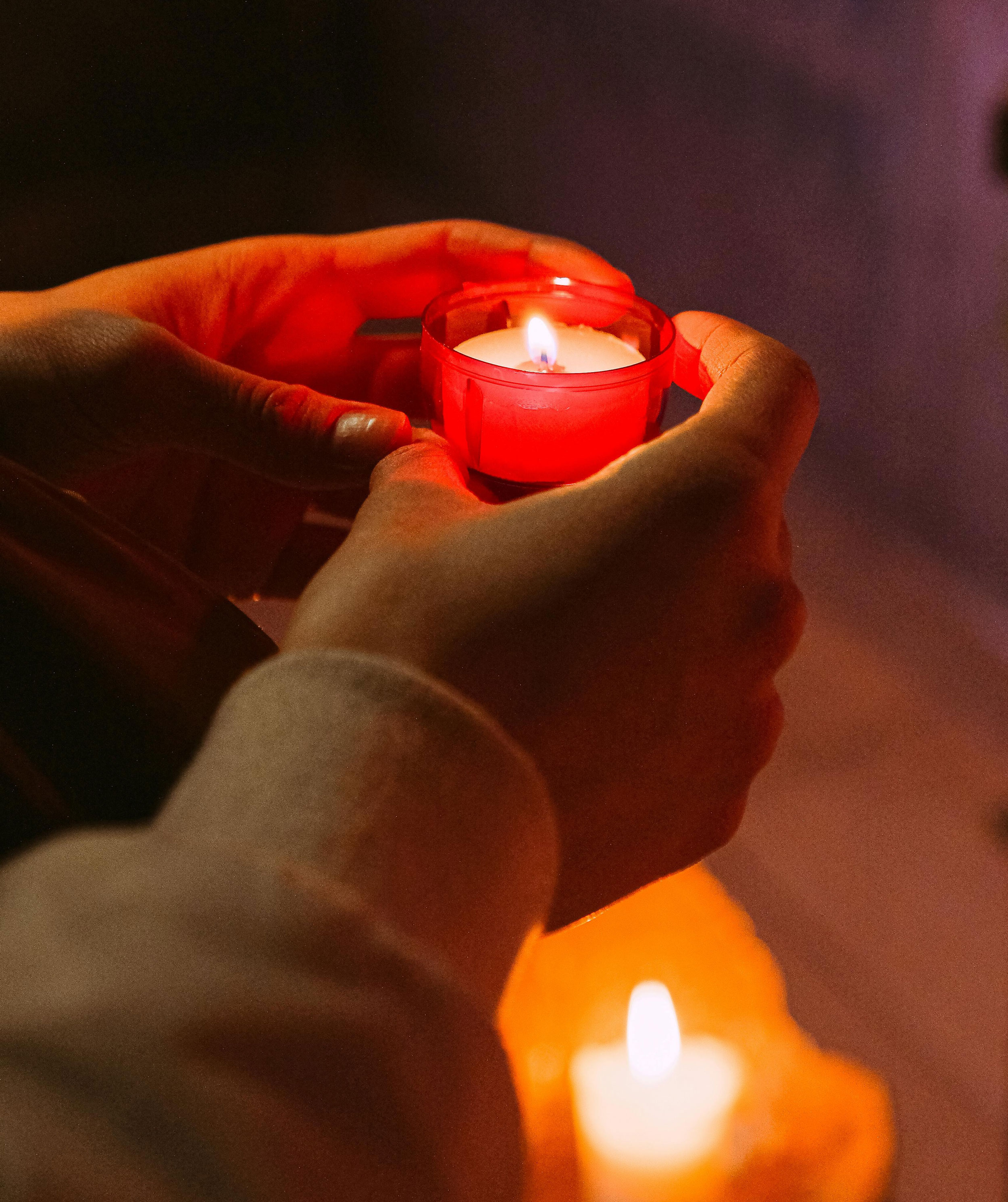 Två händer som håller i en röd ljuskopp med ett tänt ljus