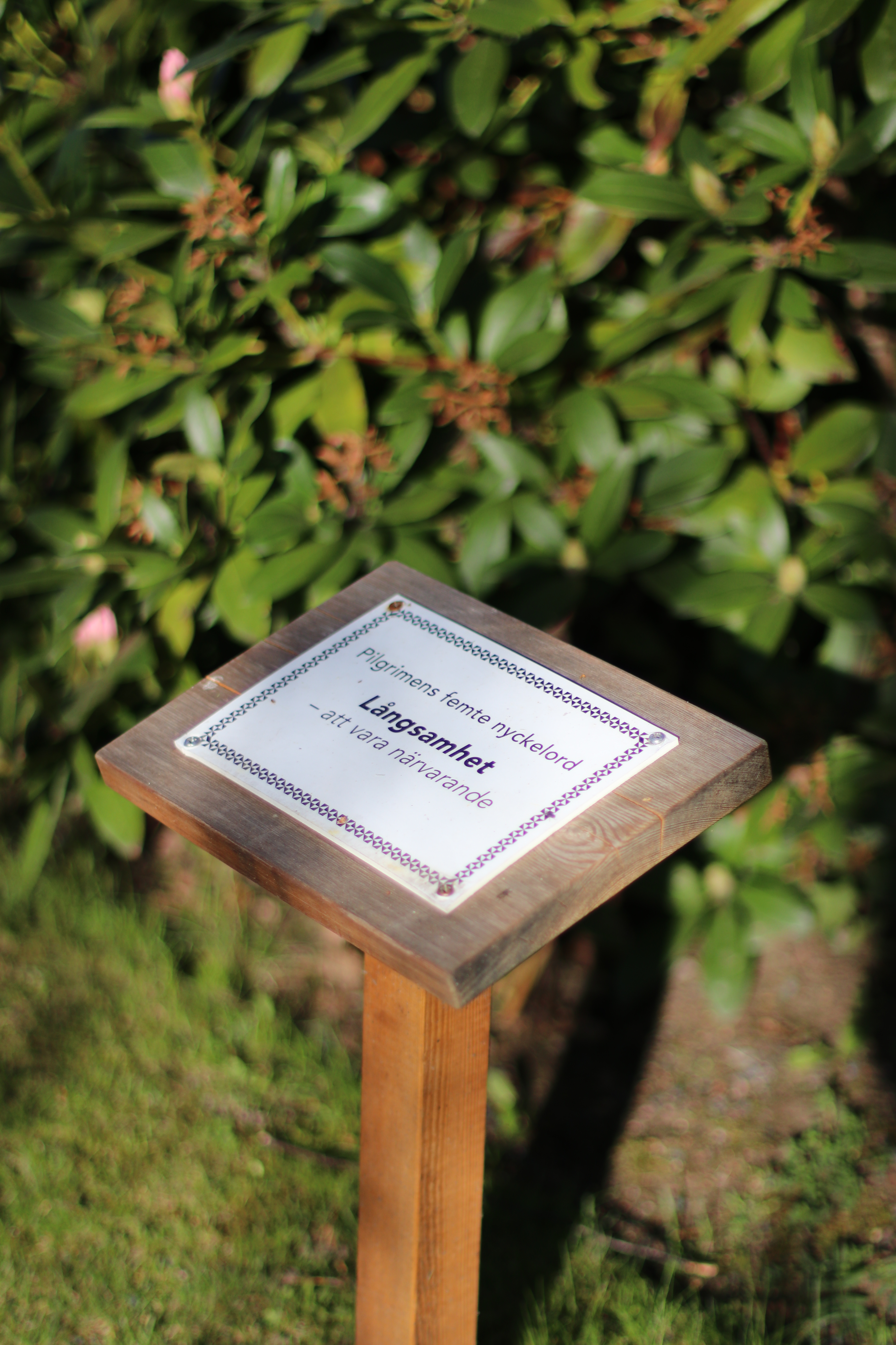 Skylt med budskapet Långsamhet, pilgrimens femte budord på pilgrimspromenaden på Huskvarna kyrkogård