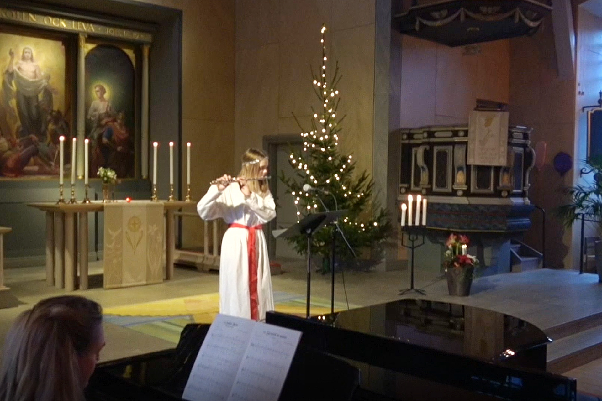 En luciaklädd flicka spelar tvärflöjt inne i Huskvarna kyrka