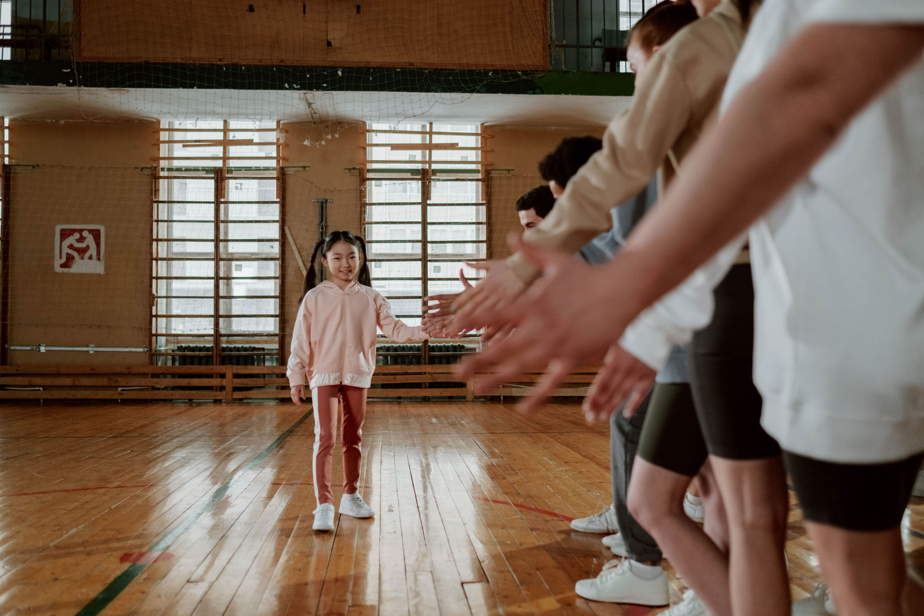 Flicka i gymnastiksal som ger high five till grupp med uträckta händer