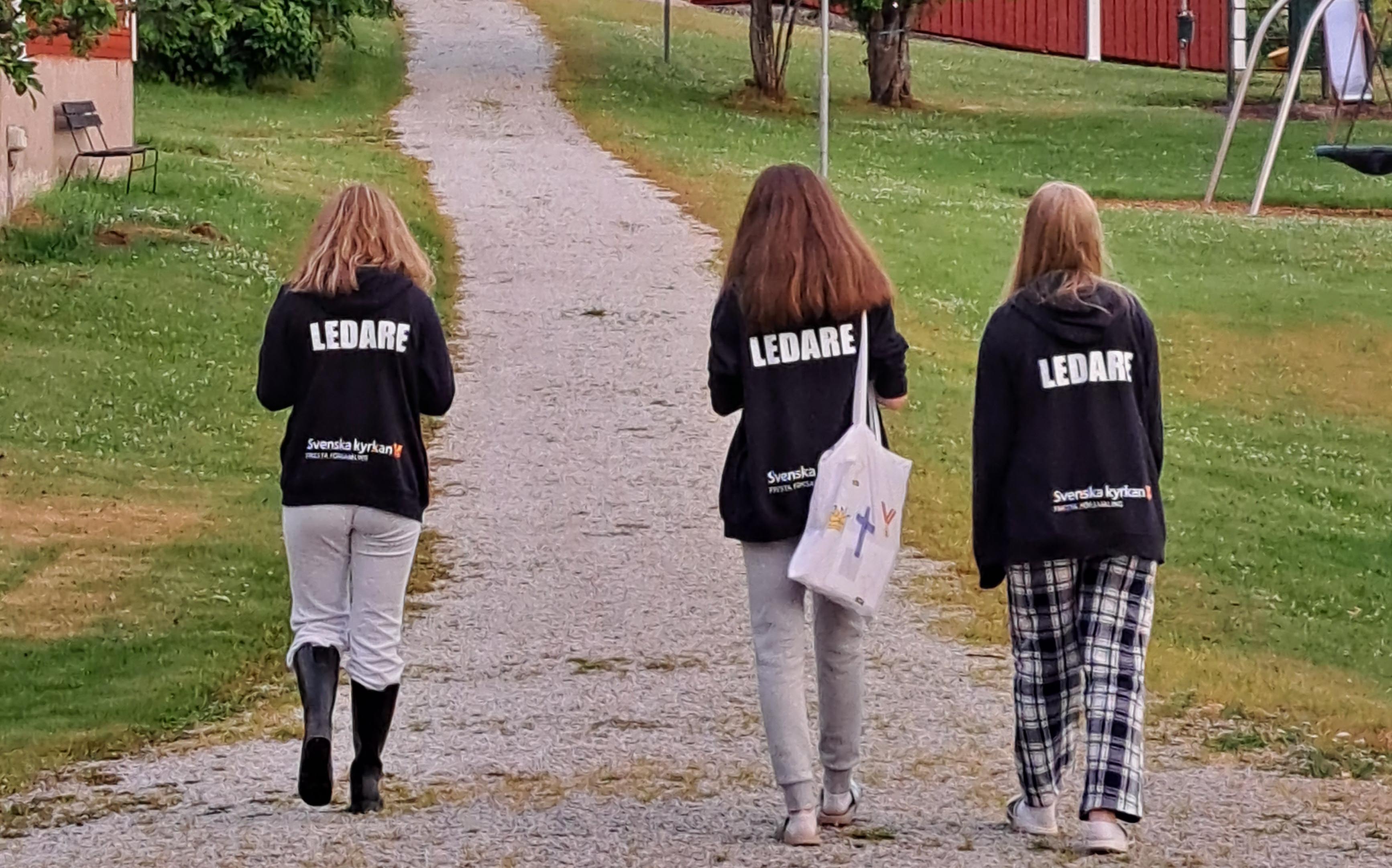 Man ser ryggen på tre ungdomar. Det står ledare på  deras tröjor.