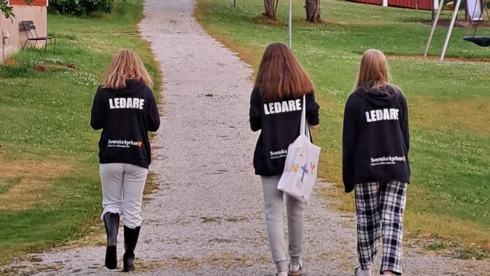 Man ser ryggen på tre ungdomar. Det står ledare på  deras tröjor.
