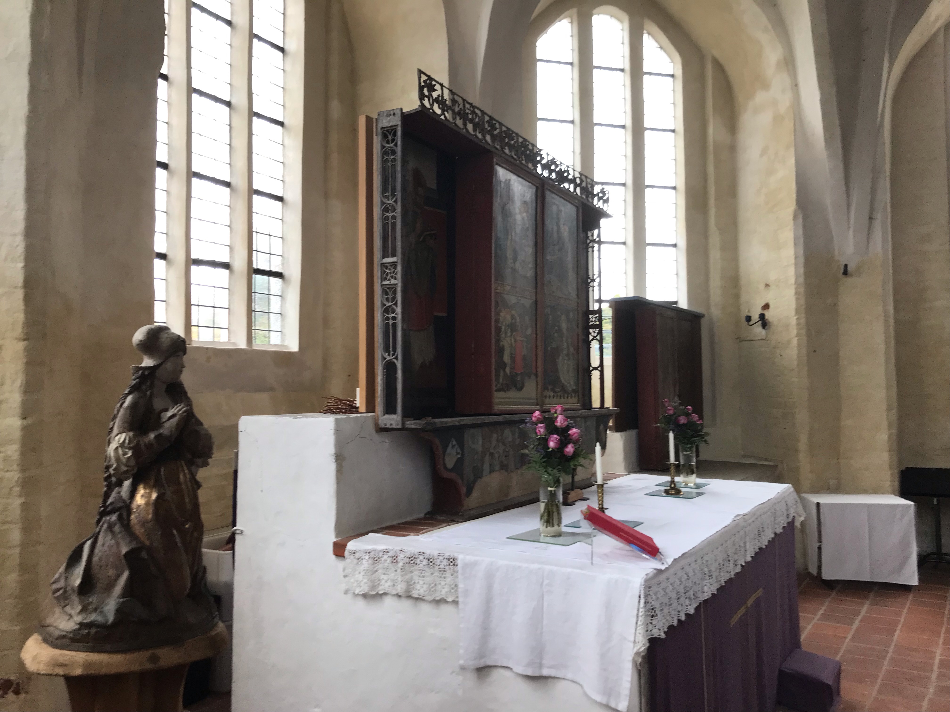 Altarskåp med stängda luckor och ett altare med blommor på.