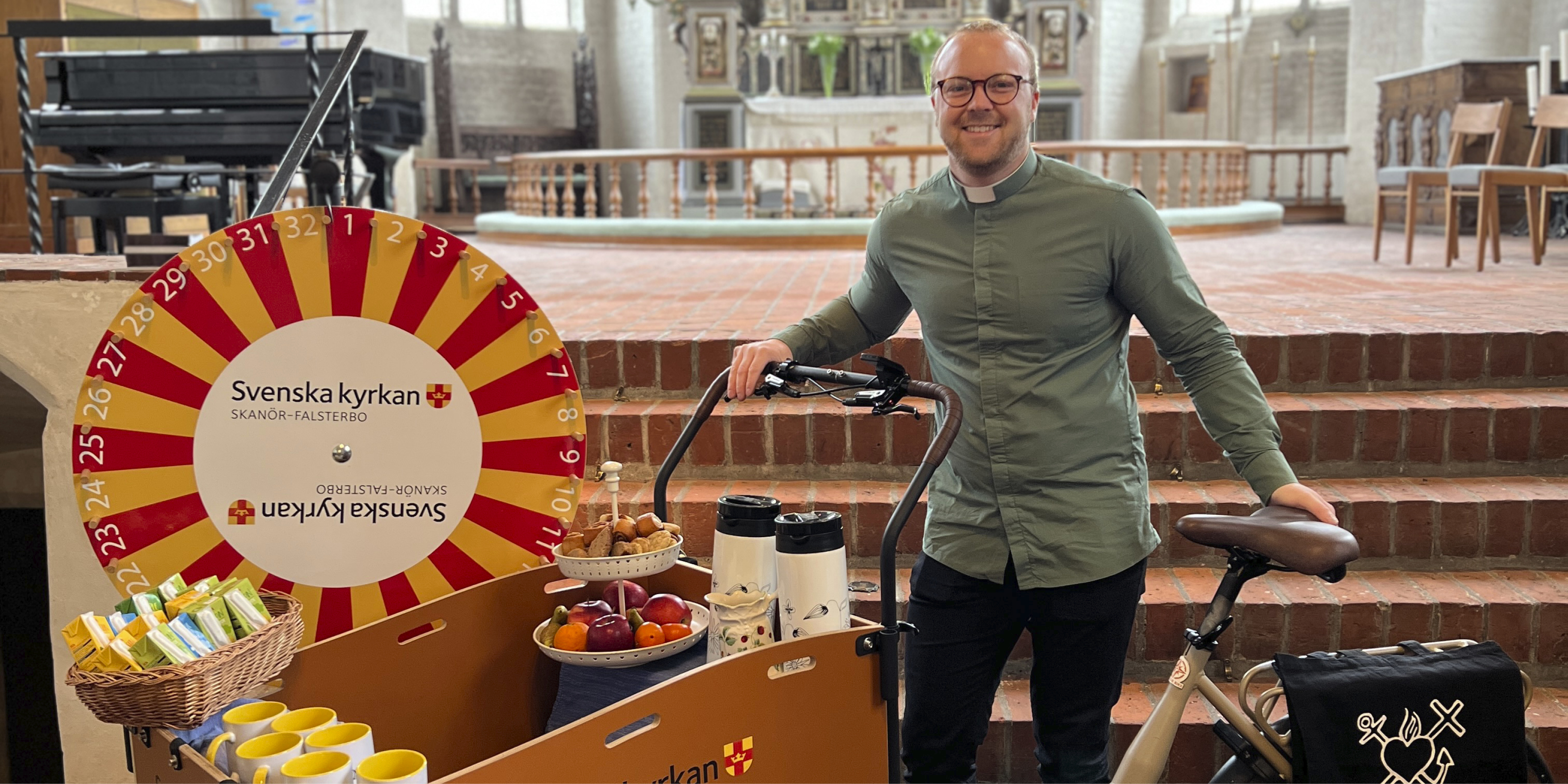 Diakon Jesper Wetterlin står vid en lådcykel i Skanörs kyrka. 