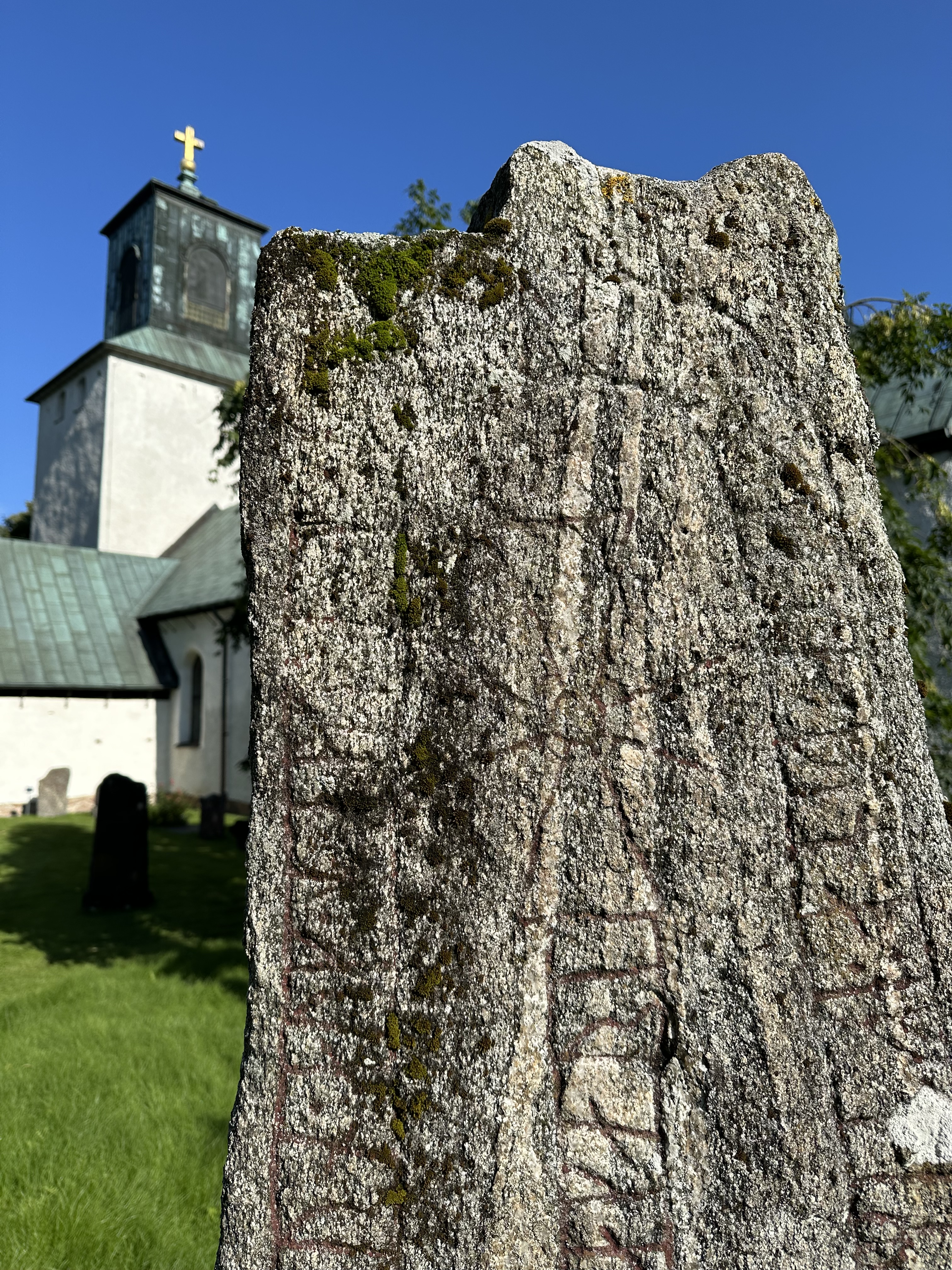 En runsten med pånga kyrka i bakgrunden