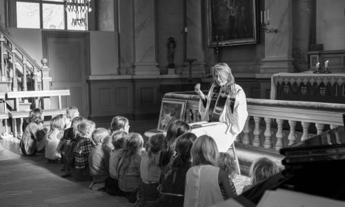 Präst sitter framför barn i kyrkan