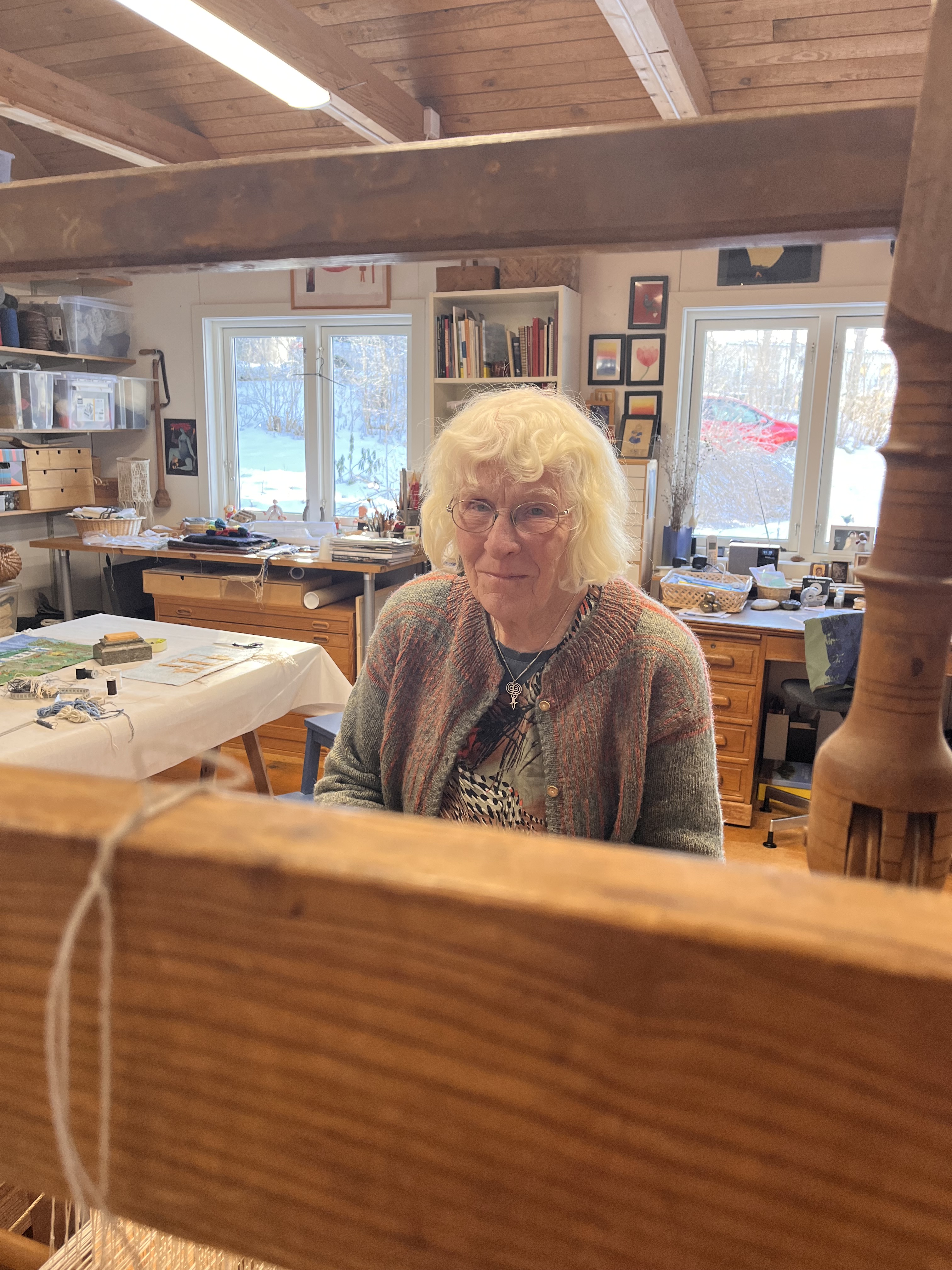 Kvinna som är konstnär sitter vid en gammal vävstol i en ateljé.