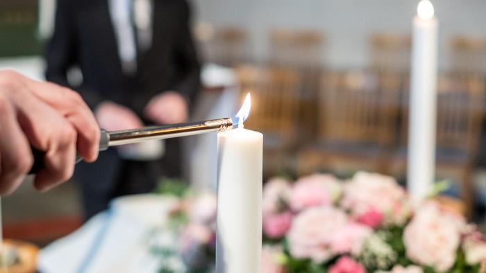 Bild på kista med rosa blommor och ljus som tänds runt om.