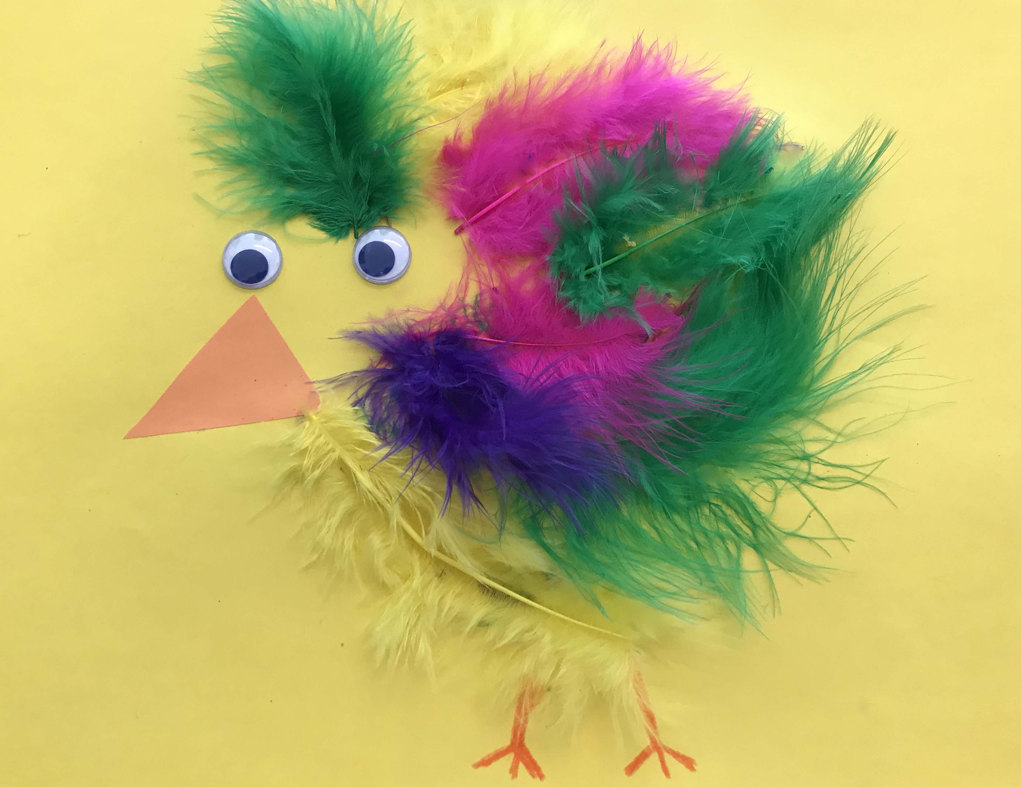 Påskpyssel i form av en kyckling gjord i fjädrar klistrad på ett gult papper.