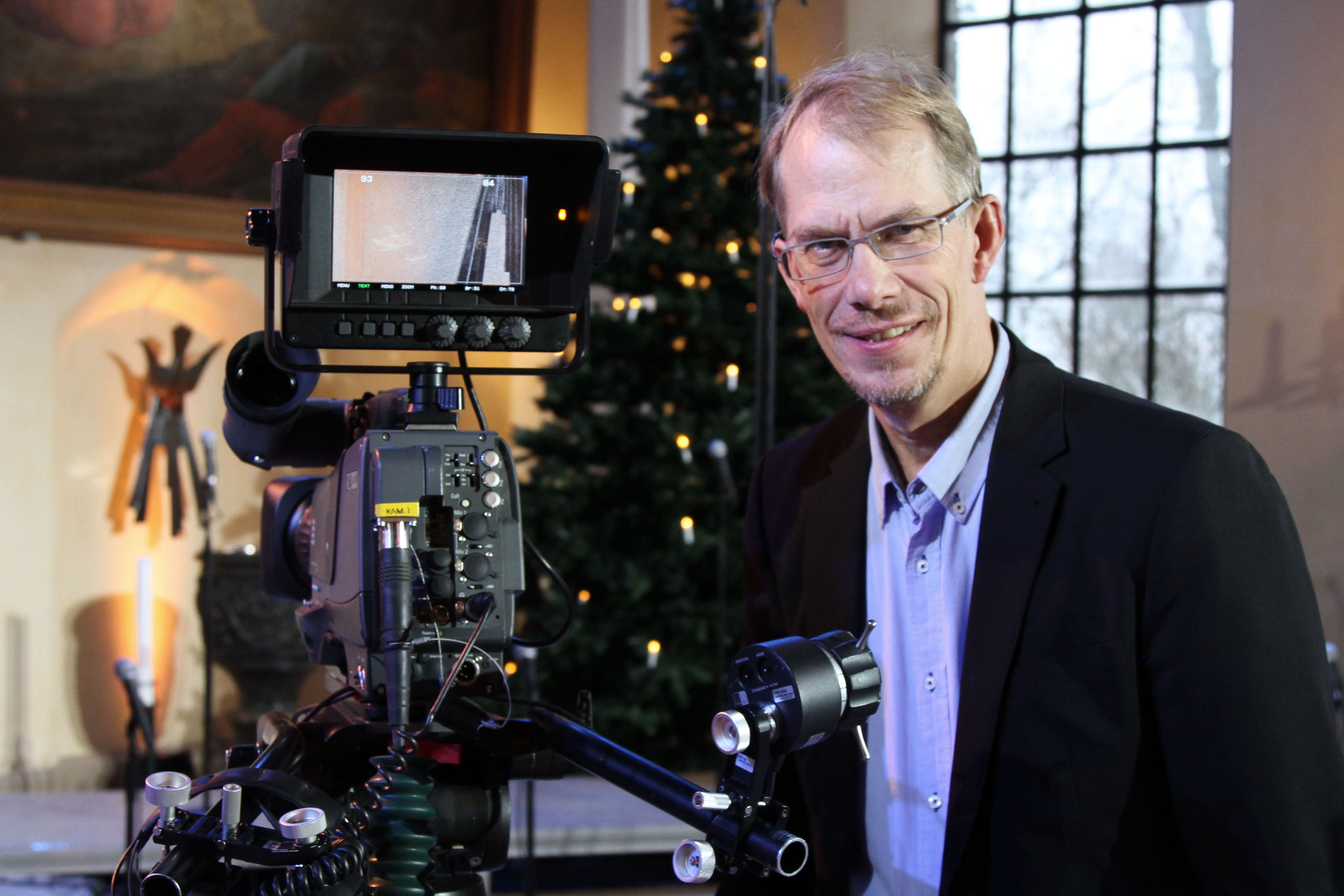 En man som är präst och tvproducent står vid en filmkamera