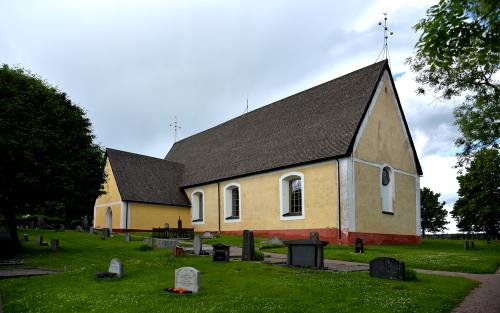 En gul kyrka utan torn. I förgrunden gräsmatta med några gravar. 
