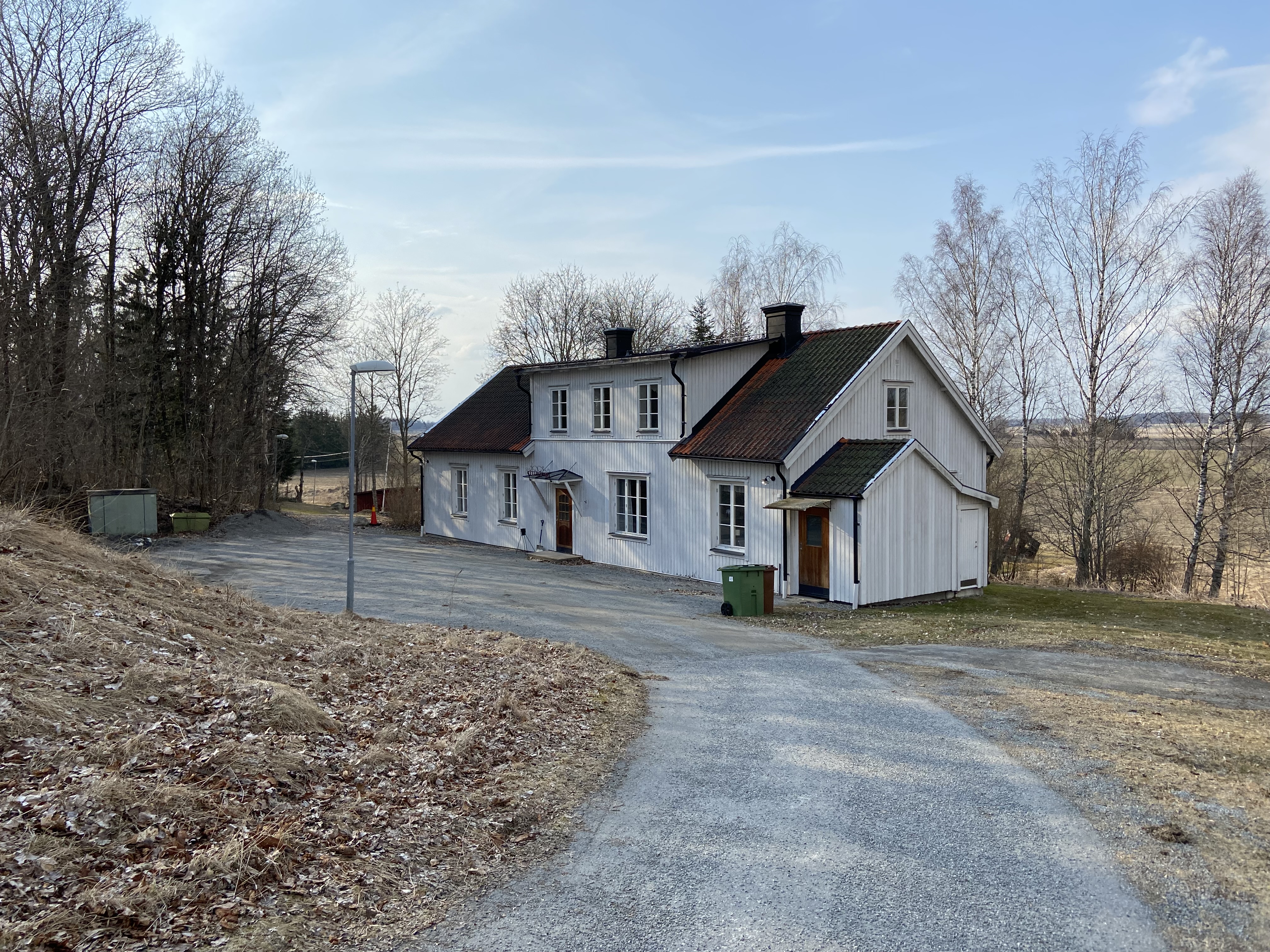 En grusväg leder ner till ett vitt hus.