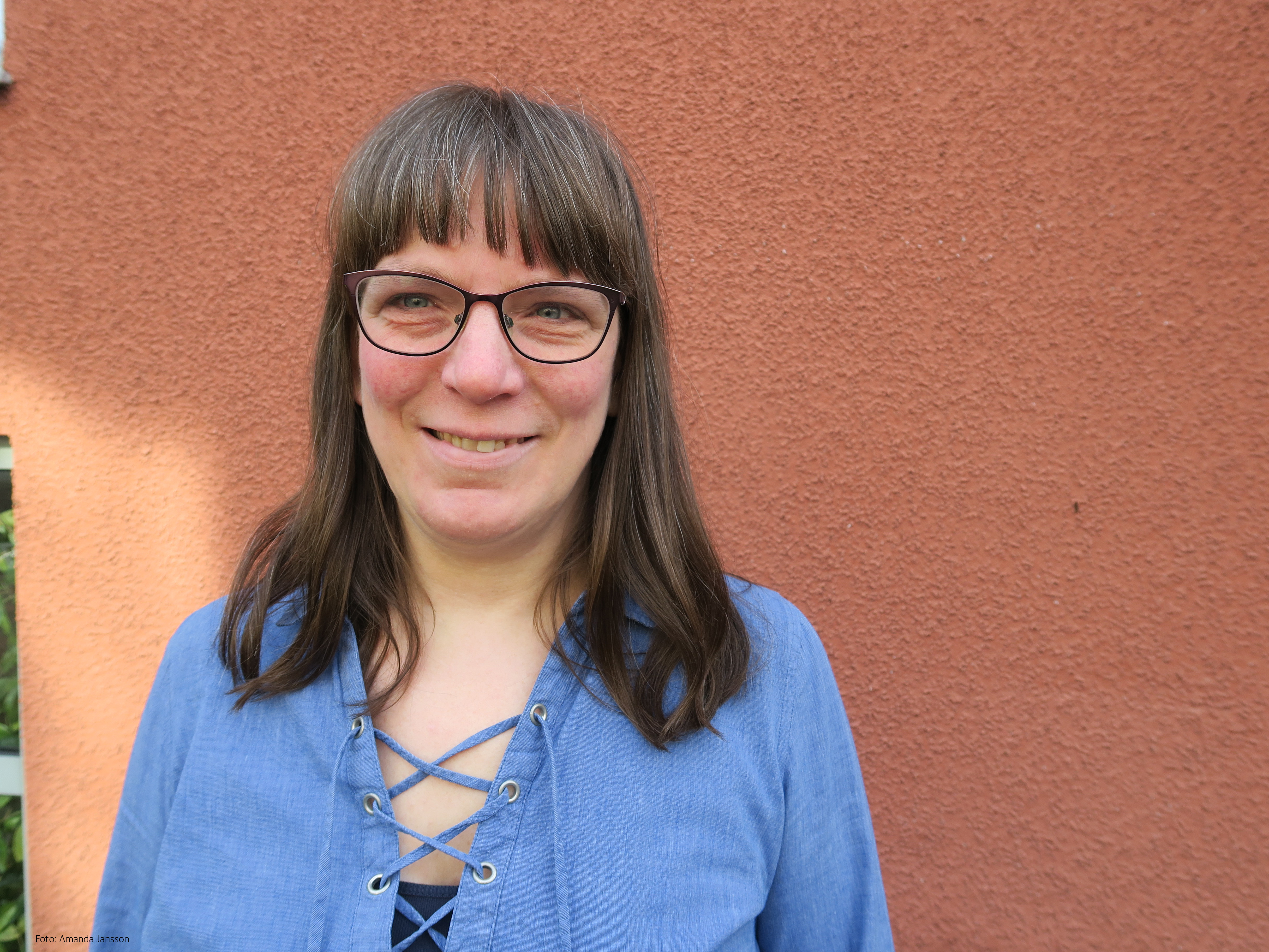 En kvinna med glasögon och mörkbrunt hår ler mot kameren.