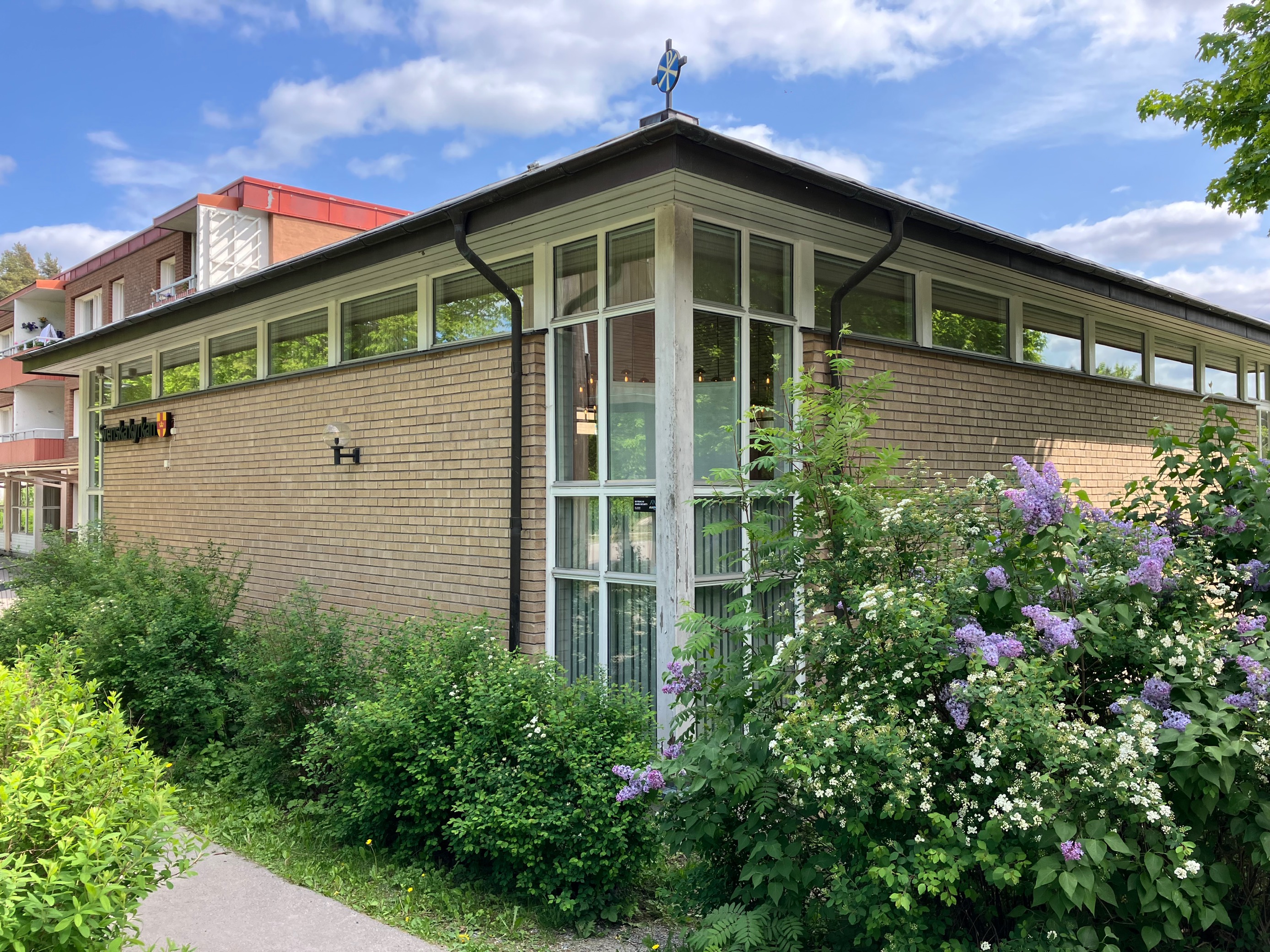 En gul tegelbyggnad omgiven av grönskande syréner.