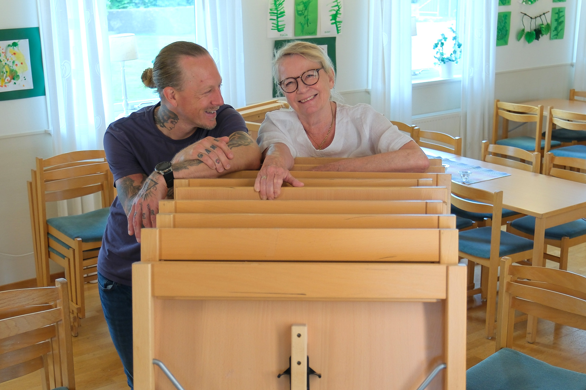 Volontärer i muskelkraft-gruppen lutar sig över staplade bord.