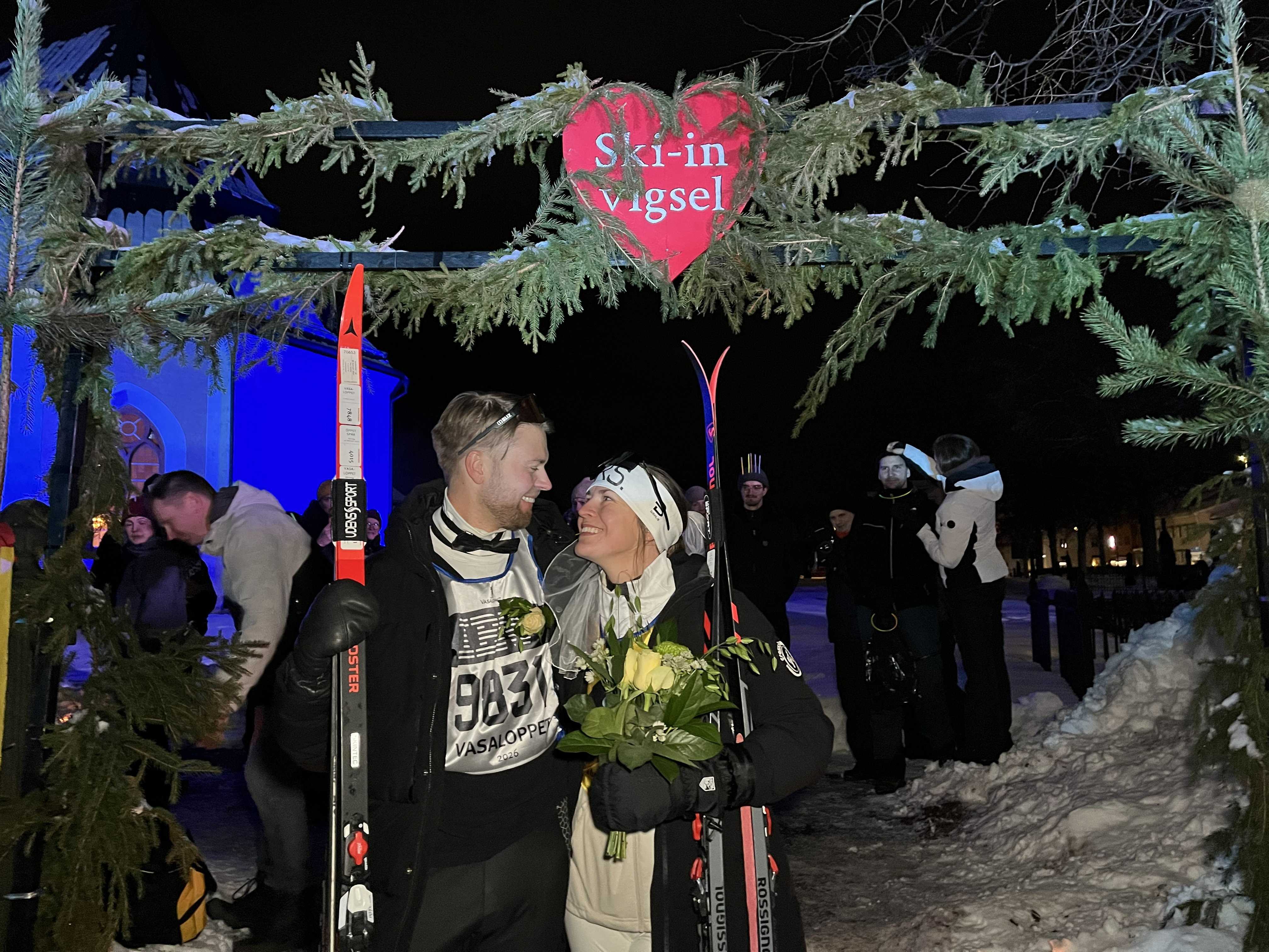 ett vigselpar står under ski in vigselbågen och tittar kärleksfullt på varandra